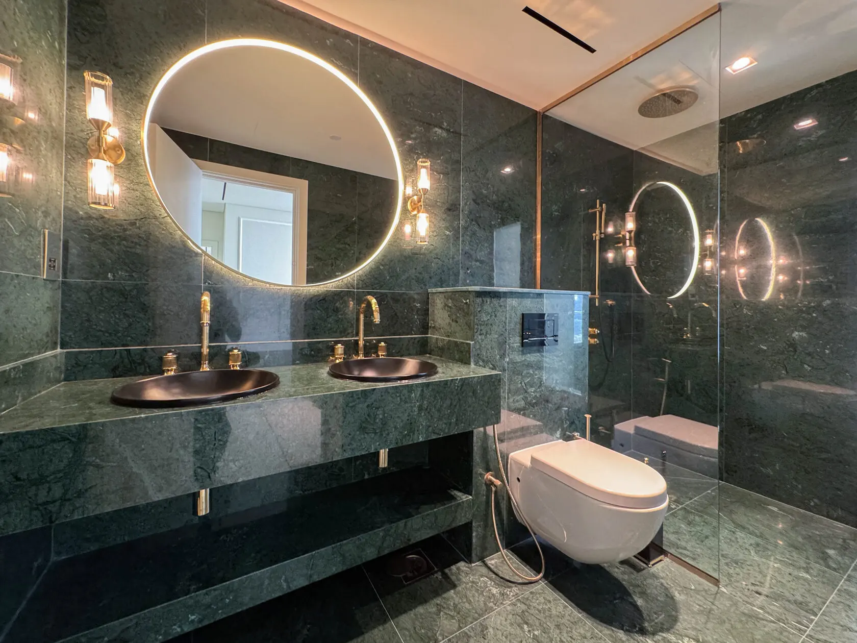 Green marble bathroom with illuminated round mirrors and twin basins in a Dubai apartment