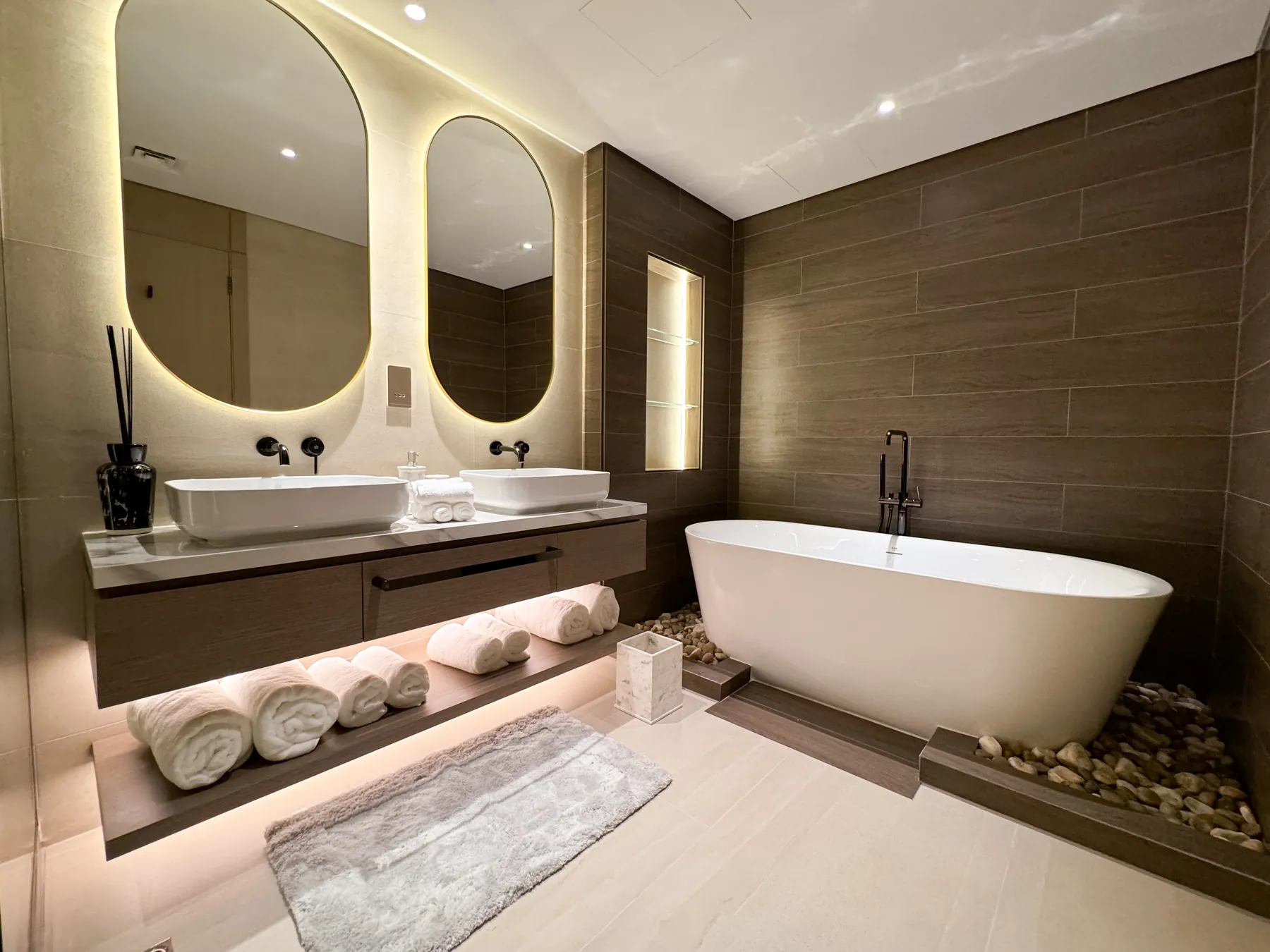 Bathroom with freestanding bath, twin basins and backlit mirrors above timber joinery